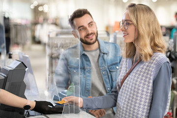 Poster - A man and a woman paying for clothes during shopping in department store