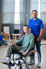 Canvas Print - Happy young male volunteer standing next to guy in a wheelchair