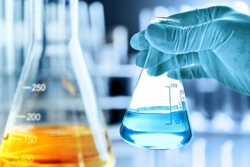 Wall Mural - hand of scientist holding flask with lab glassware in chemical laboratory background, science labora
