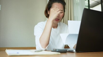 Wall Mural - slow motion scene of young asian woman feeling headache while list of expense after calculated about money by calculator at desk with financial bill for millennial lifestyle and financial concept