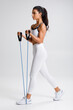 © nikolas_jkd - Fitness woman working out with resistance band on gray background. Athletic girl exercises with expander