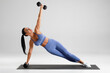 © nikolas_jkd - Fitness woman doing side plank exercise on gray background. Athletic girl working out with dumbbells