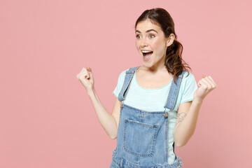 Wall Mural - Young fun overjoyed excited happy caucasian woman in trendy denim clothes blue tshirt do winner gesture clench fist scream isolated on pastel pink background studio portrait. People lifestyle concept