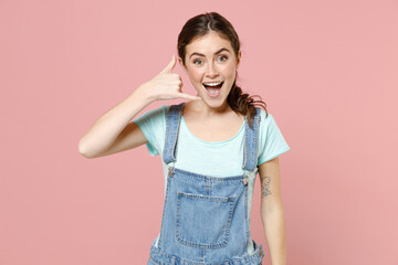 Wall Mural - Young excited cheerful caucasian woman in trendy denim clothes blue t-shirt doing phone gesture like says call me back isolated on pastel pink background studio portrait. People lifestyle concept.