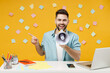 Young successful employee business man in shirt sit work at white office desk with pc laptop scream shout aside in megaphone point index finger aside on workspace isolated on yellow background studio.