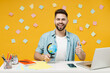 Young employee geography student teacher business man in shirt sit work at white office desk pc laptop hold Earth world globe show thumb up like gesture isolated on yellow background studio portrait.
