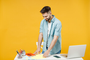 Canvas Print - Young fun smiling happy successful employee business man wear casual blue shirt stand work at white office desk with laptop isolated on yellow background studio portrait. Achievement career concept.