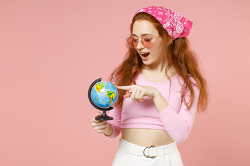 Young traveler gography student teacher caucasian woman in rose clothes bandana glasses spin touch Earth world globe choose country isolated on pastel pink background studio People lifestyle concept.