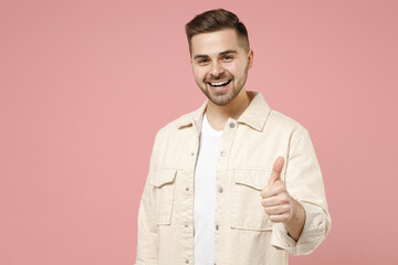 Young smiling happy positive satisfied trendy fashionable caucasian man in jacket white t-shirt show thumb up like gesture isolated on pastel pink background studio portrait. People lifestyle concept.