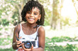 © Djavan Rodriguez - young african american toddler girl holding an old camera and looking at camera.