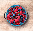 Berries mix fresh assortment ready to eat arrangement in rustic old blue metal plate on old kitchen wooden table overhead studio shot