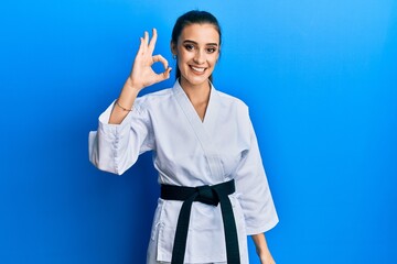 Wall Mural - Beautiful brunette young woman wearing karate fighter uniform with black belt smiling positive doing ok sign with hand and fingers. successful expression.