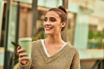 Wall Mural - Beautiful brunette woman smiling happy and confident outdoors at the city on a sunny day of autumn drinking a take away cup of coffee