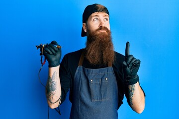 Wall Mural - Redhead man with long beard tattoo artist wearing professional uniform and gloves pointing up looking sad and upset, indicating direction with fingers, unhappy and depressed.