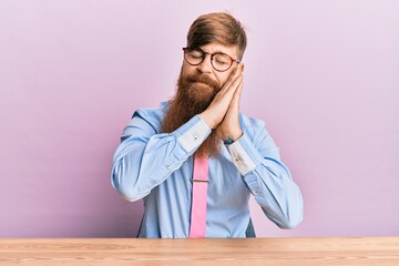 Wall Mural - Young irish redhead man wearing business shirt and tie sitting on the table sleeping tired dreaming and posing with hands together while smiling with closed eyes.