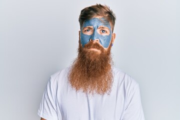 Sticker - Young irish redhead man wearing facial mask with serious expression on face. simple and natural looking at the camera.