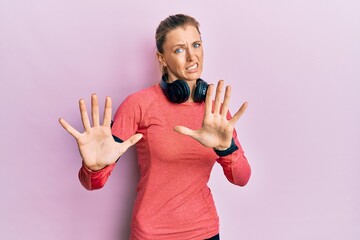 Canvas Print - Beautiful caucasian woman wearing sportswear and arm band afraid and terrified with fear expression stop gesture with hands, shouting in shock. panic concept.