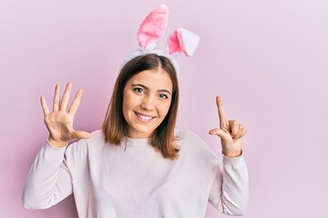 Canvas Print - Young beautiful woman wearing cute easter bunny ears showing and pointing up with fingers number seven while smiling confident and happy.