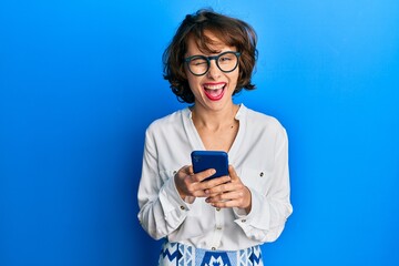 Canvas Print - Young brunette woman using smartphone winking looking at the camera with sexy expression, cheerful and happy face.