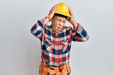 Wall Mural - Senior hispanic man wearing handyman uniform suffering from headache desperate and stressed because pain and migraine. hands on head.