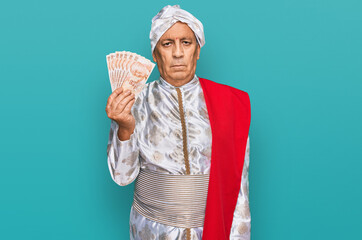 Wall Mural - Senior hispanic man wearing sherwani costume holding 50 indian rupee banknotes thinking attitude and sober expression looking self confident