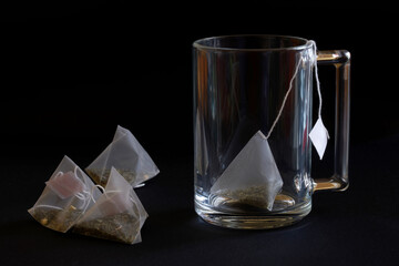 Wall Mural - Pyramid tea bags with green tea and a glass transparent mug on a black background