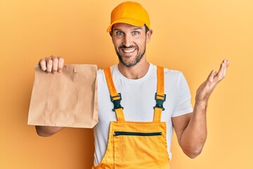 Sticker - Young handsome delivery man holding take away paper bag celebrating achievement with happy smile and winner expression with raised hand