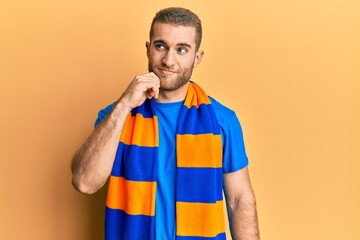 Wall Mural - Young caucasian man football hooligan cheering game thinking concentrated about doubt with finger on chin and looking up wondering