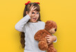 Little caucasian girl kid hugging teddy bear stuffed animal smiling happy doing ok sign with hand on eye looking through fingers