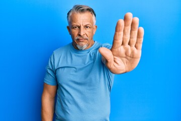 Canvas Print - Middle age grey-haired man wearing casual clothes doing stop sing with palm of the hand. warning expression with negative and serious gesture on the face.