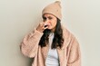 © Krakenimages.com - Young hispanic woman wearing wool sweater and winter hat smelling something stinky and disgusting, intolerable smell, holding breath with fingers on nose. bad smell