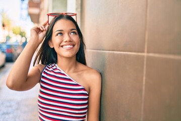 Sticker - Young latin girl smiling happy leaning on the wall at the city.