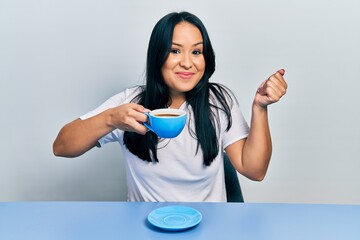 Wall Mural - Beautiful hispanic woman with nose piercing drinking a cup coffee screaming proud, celebrating victory and success very excited with raised arm