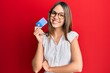 Young brunette woman holding credit card smiling with a happy and cool smile on face. showing teeth.