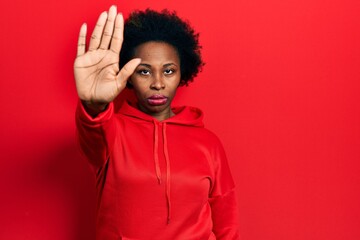 Young african american woman wearing casual sweatshirt doing stop sing with palm of the hand. warning expression with negative and serious gesture on the face.