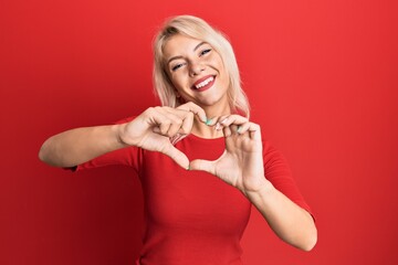 Sticker - Young blonde girl wearing casual clothes smiling in love doing heart symbol shape with hands. romantic concept.