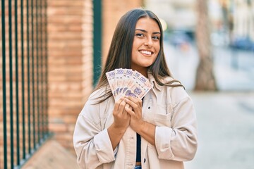 Wall Mural - Young hispanic girl smiling happy holding mexican 500 pesos banknotes at the city.