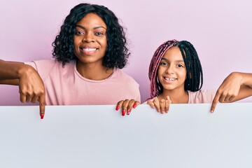 Wall Mural - Beautiful african american mother and daughter holding blank empty banner smiling happy pointing with hand and finger