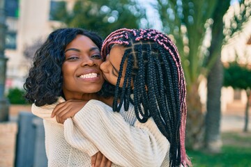 Sticker - Beautiful african american mother giving daughter piggyback ride and kissing at the park.