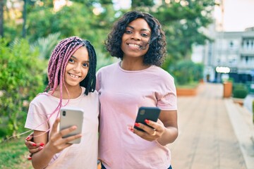 Sticker - African american mother and daugther hugging and using smartphone at the park.