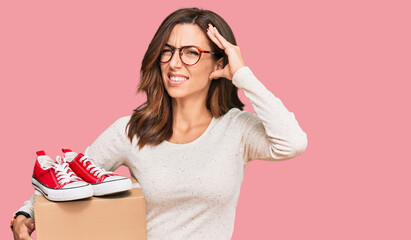 Canvas Print - Young brunette woman holding box with red casual shoes stressed and frustrated with hand on head, surprised and angry face