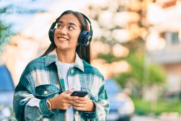 Poster - Young latin girl smiling happy using smartphone and headphones at the city.