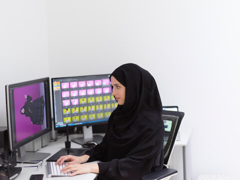 Muslim female graphic designer working on computer using graphic tablet and two monitors