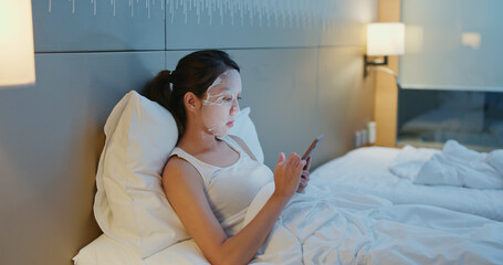 Poster - Woman apply face mask and use of mobile phone on bed at night