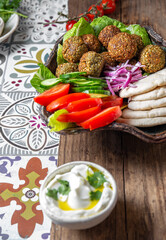 Wall Mural - Falafel, fresh vegetables and pita bread on clay plate, gray background