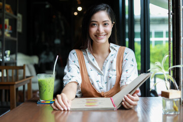 Asian woman open menu for ordering in coffee cafe and restaurant and smiling for happy time