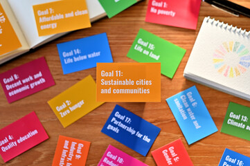 There is a card with the statement Goal 11:Sustainable cities and communities on table one of the goals of the SDGs and a symbol.