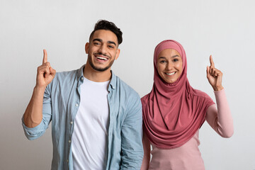 Wall Mural - Idea Concept. Cheerful young muslim couple pointing fingers up