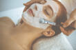 © rogerphoto - Beautiful brunette woman enjoying applying cosmetic mask with closed eyes. Relaxing treatment in medicine and spa concepts