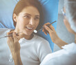 © rogerphoto - Smiling brunette woman being examined by dentist at dental clinic. Hands of a doctor holding dental instruments near patient's mouth. Healthy teeth and medicine concept